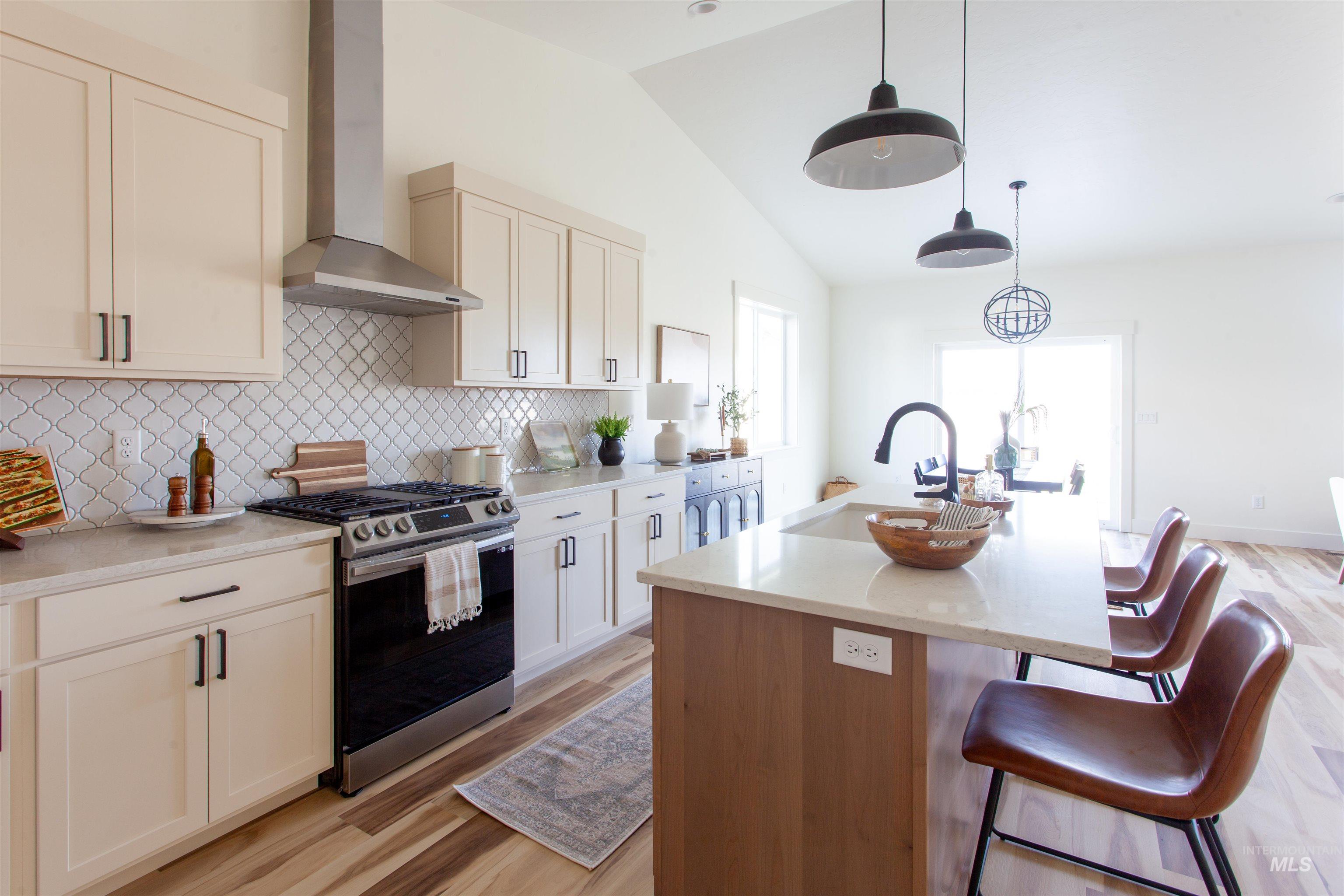 1113 Velvet Loop Wilder, ID 83676 - Photo 11 of 29 Kitchen with wall chimney range hood, stainless steel range with gas cooktop, a center island with sink, light wood-type flooring, and decorative backsplash