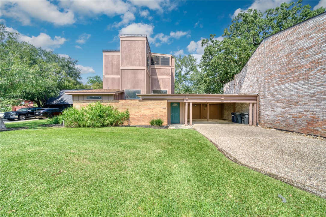 View of front of property featuring a front lawn, brick siding, an attached carport, a patio, and driveway