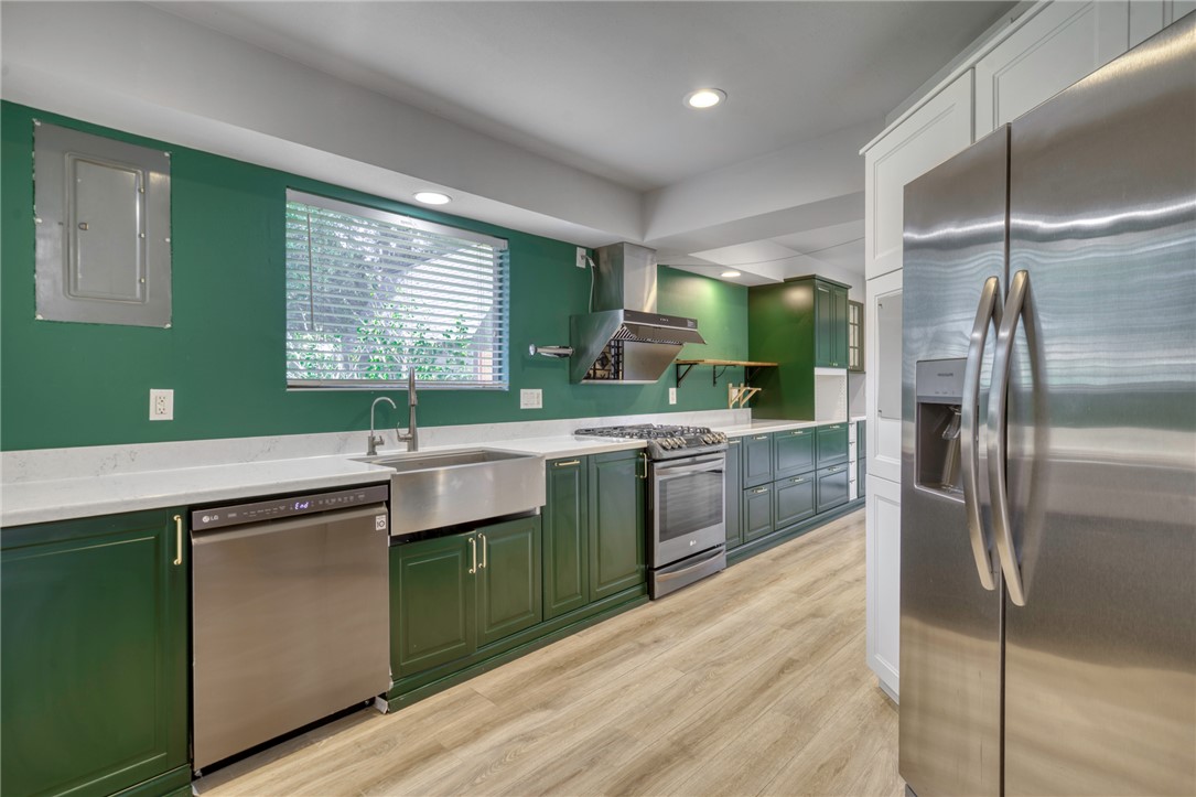 1513 Wolf Run College Station, TX 77840 - Photo 12 of 33 Kitchen featuring green cabinetry, appliances with stainless steel finishes, wall chimney exhaust hood, electric panel, and light wood-type flooring