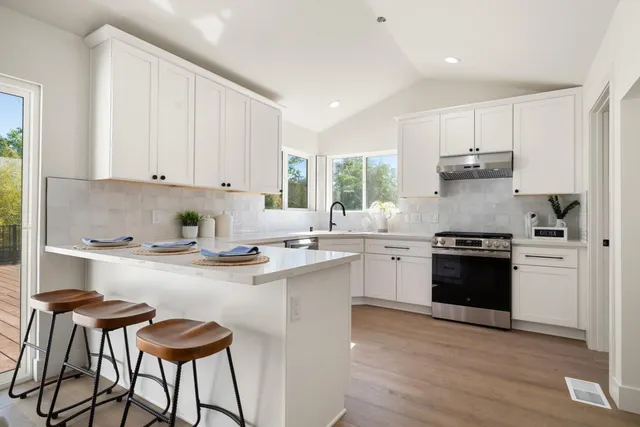 a kitchen with stainless steel appliances granite countertop a stove a sink dishwasher and white cabinets with wooden floor