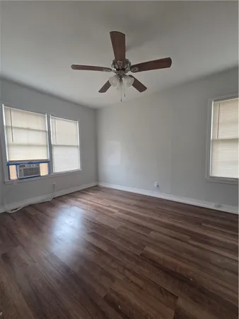 an empty room with wooden floor fan and windows