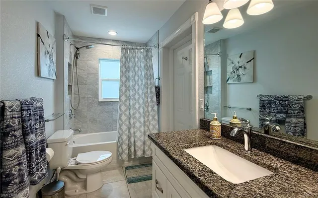 a bathroom with a granite countertop sink a toilet a mirror a bathtub and shower