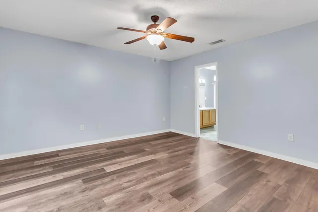 a view of an empty room with wooden floor and a ceiling fan