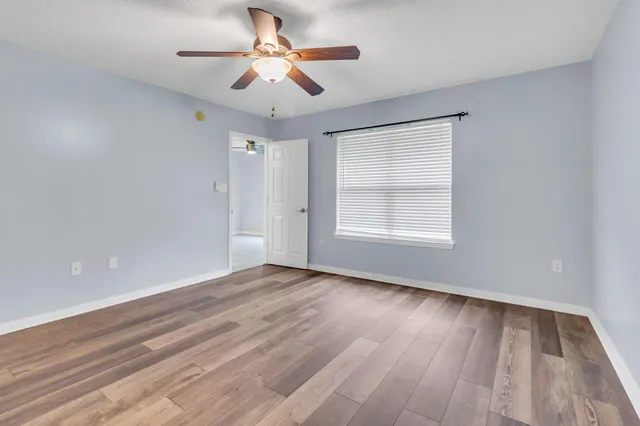 an empty room with wooden floor ceiling fan and windows