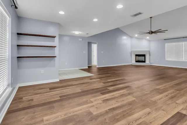 an empty room with wooden floor fireplace and ceiling fan