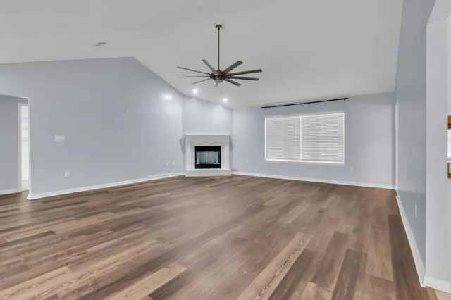 an empty room with wooden floor ceiling fan and windows