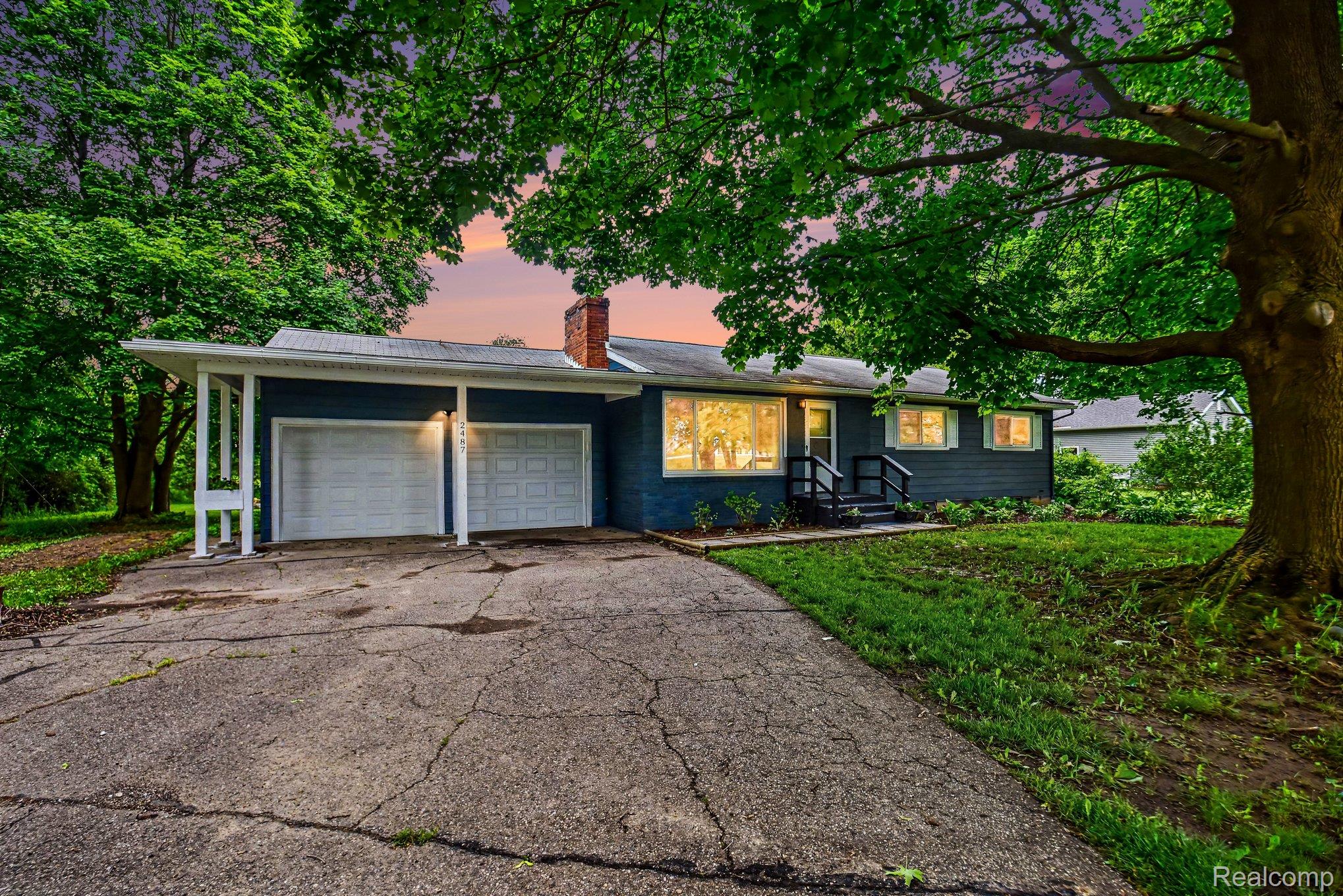 2487 North Lapeer Road Lapeer, MI 48446 - Photo 1 of 16 Ranch-style exterior with dark blue siding, a prominent brick chimney, and a covered two-car garage