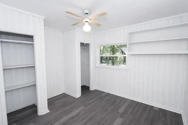 an empty room with wooden floor chandelier fan and windows