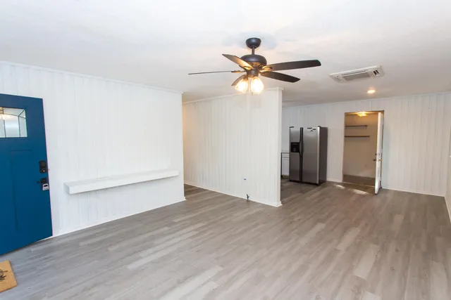 a view of an empty room with wooden floor and a ceiling fan