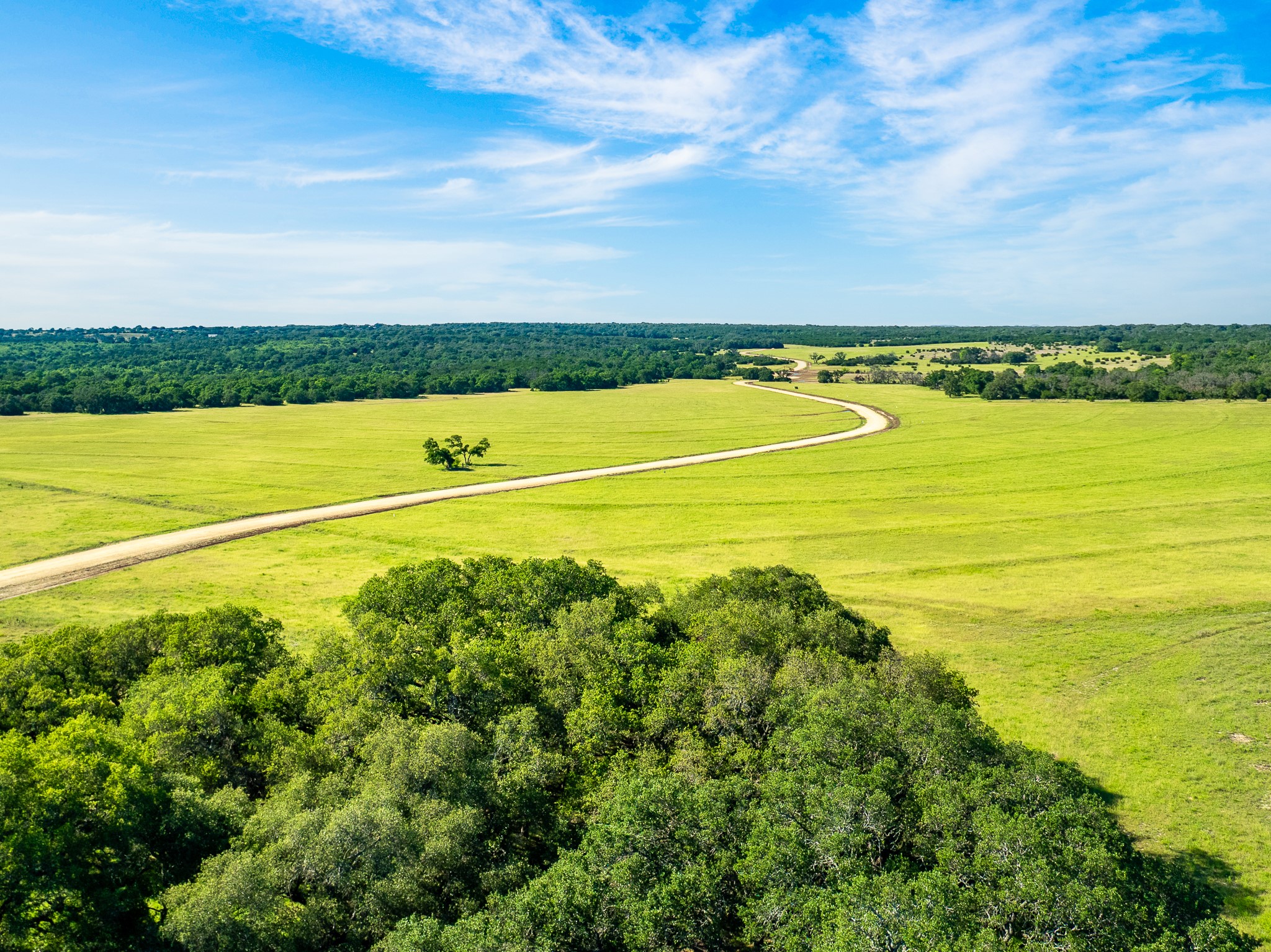 32 Feild Ranch Road Burnet, TX 78611 - Photo 5 of 40 Vast green fields stretch endlessly, bordered by a meandering road under an expansive blue sky.