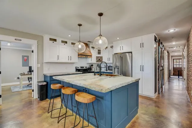 a large kitchen with stainless steel appliances kitchen island granite countertop a table chairs and a refrigerator