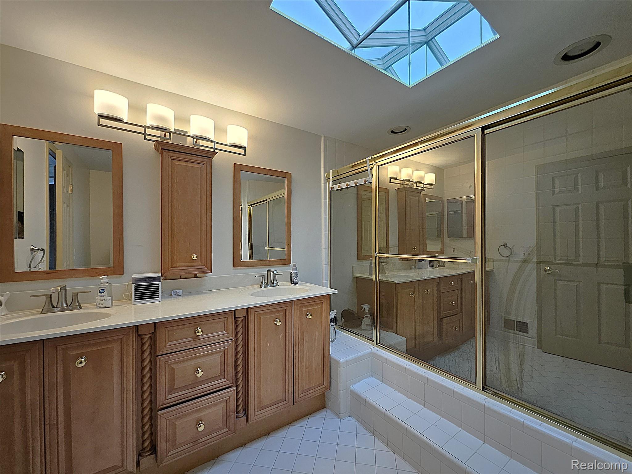 1114 Chaffer Drive Rochester, MI 48306 - Photo 41 of 50 Bathroom featuring a skylight, dual vanity with light wood cabinetry, white countertops, and a shower-tub combination with a glass enclosure