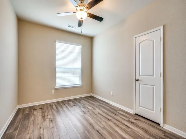 an empty room with wooden floor fan and windows