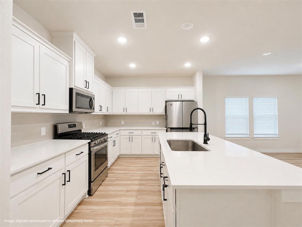 631 Cari Lane Forney, TX 75126 - Photo 5 of 17 Kitchen featuring white cabinetry, stainless steel appliances, white countertops, a central island with an undermount sink, and wood-finish flooring