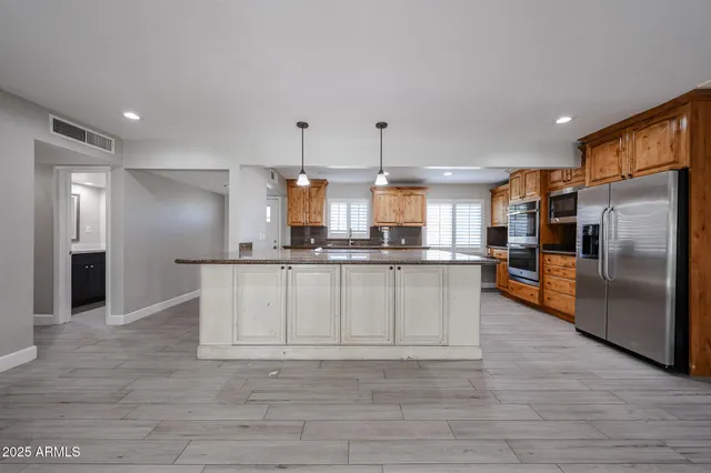 a large kitchen with stainless steel appliances kitchen island granite countertop a refrigerator a stove a sink and a oven