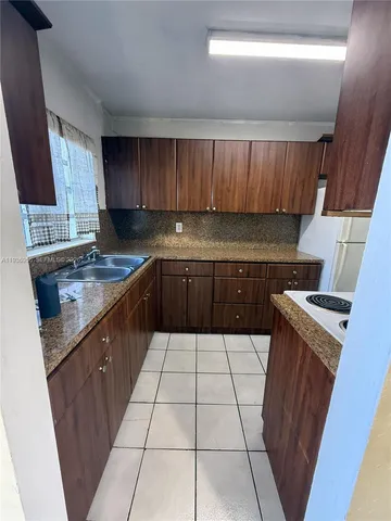 a kitchen with a sink a stove top oven a window and cabinetry