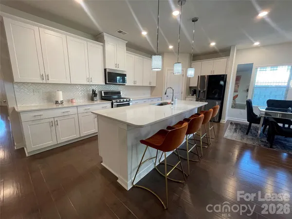a kitchen with stainless steel appliances kitchen island granite countertop a stove a sink a refrigerator and white cabinets with wooden floor