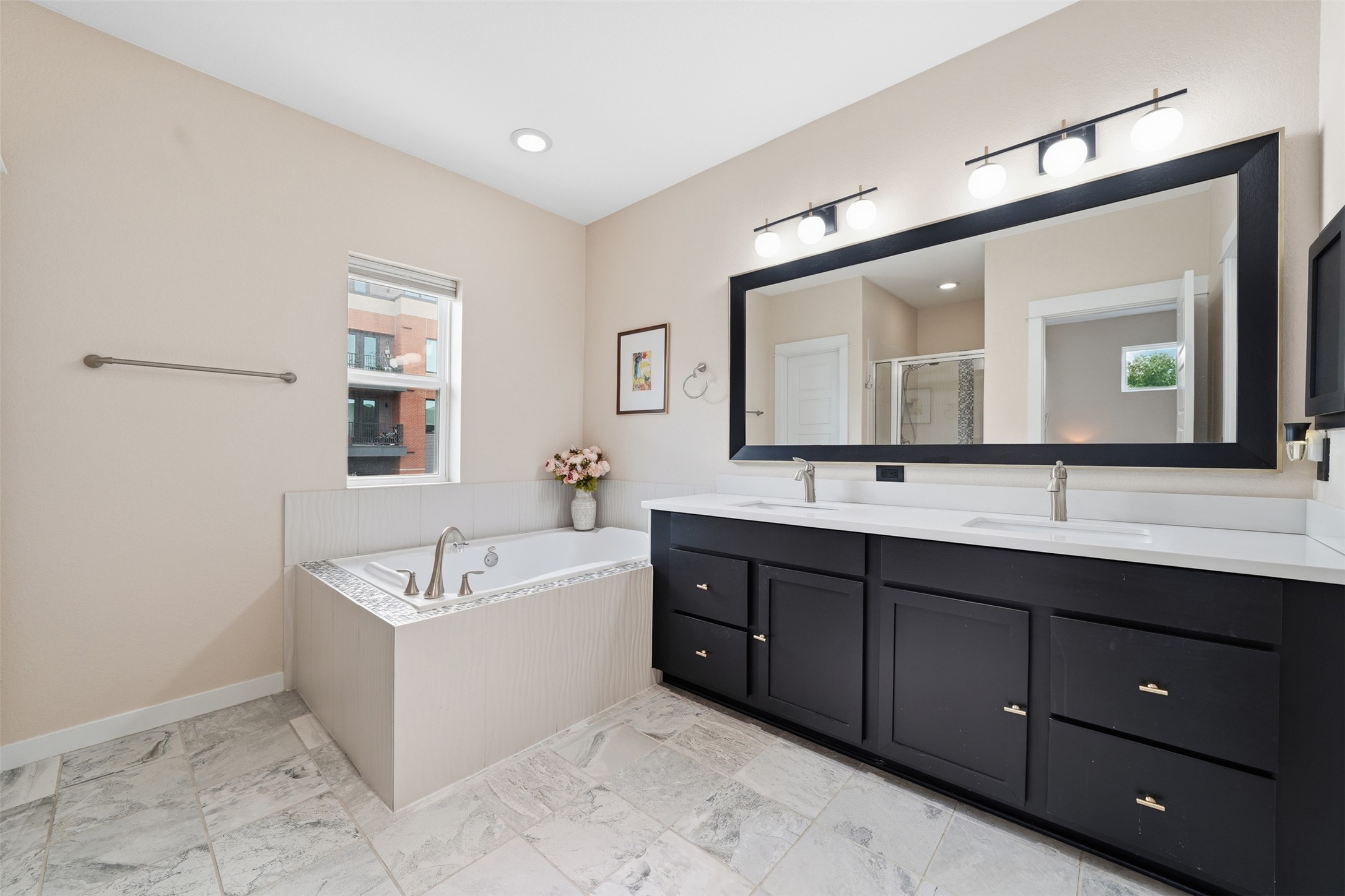 3901 Vaughan Street Austin, TX 78723 - Photo 23 of 37 Bathroom featuring a built-in tub with tile surround, a dual vanity with a white countertop and matte black cabinetry, a large framed mirror, and tile flooring