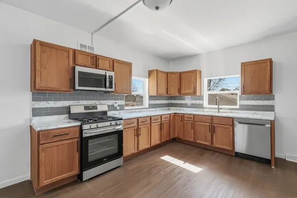 a kitchen with stainless steel appliances granite countertop a stove top oven a sink dishwasher and a microwave oven with wooden floor