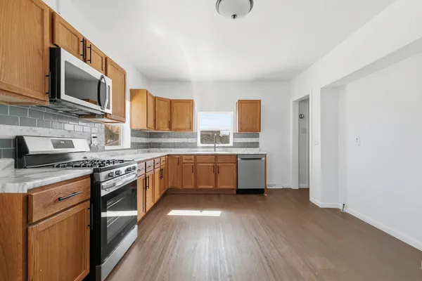 a kitchen with stainless steel appliances a sink dishwasher a stove top oven a refrigerator with wooden floors and cabinets