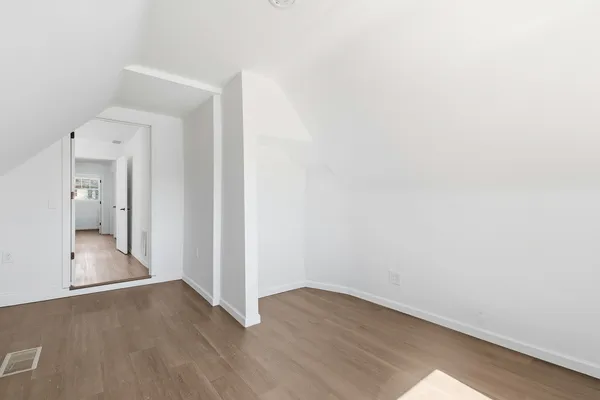 a view of a hallway with wooden floor and a bathroom