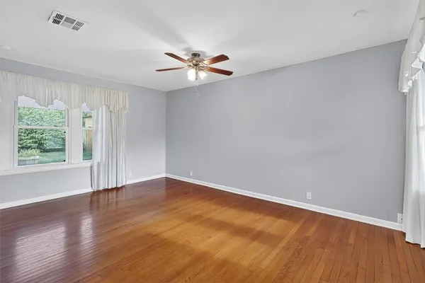an empty room with wooden floor fan and windows