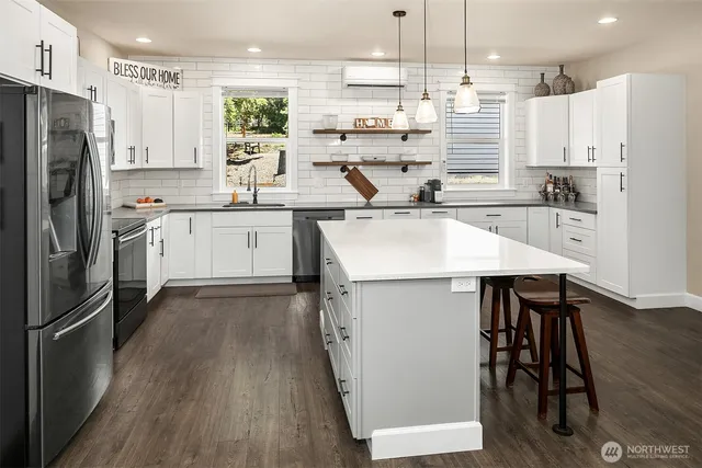 a kitchen with stainless steel appliances white cabinets a sink a stove a refrigerator and island with wooden floor