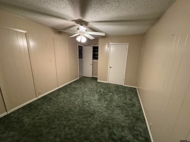 an empty room with a chandelier fan and wooden floor