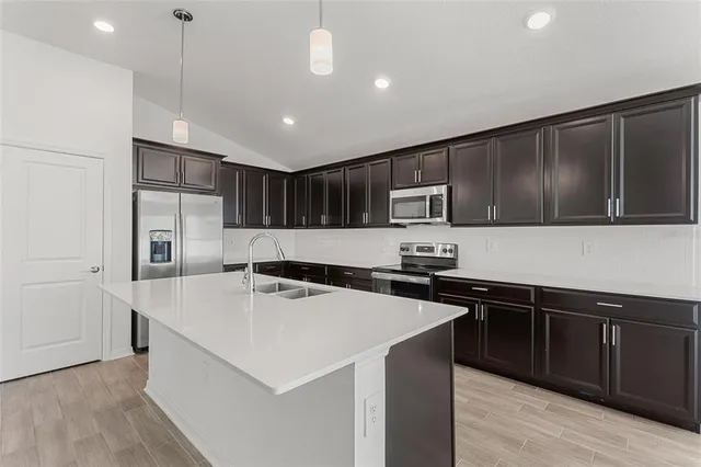 a kitchen with stainless steel appliances a sink a stove a refrigerator cabinets and wooden floor