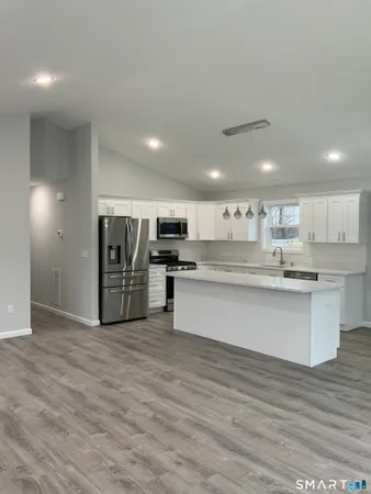 a large white kitchen with wooden floors stainless steel appliances and white cabinets