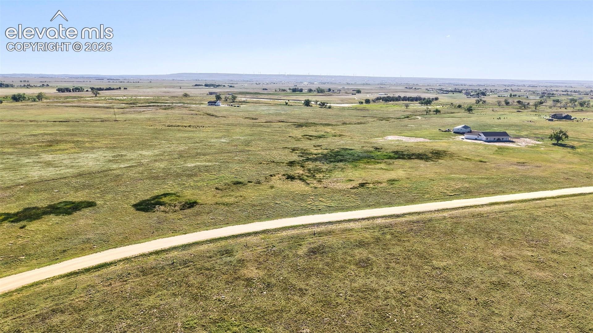 8007 Wrangler Ranch View Peyton, CO 80831 - Photo 2 of 9 Expansive open land featuring a winding dirt road and distant single-story residences