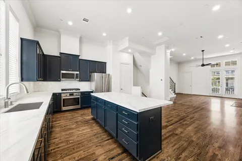 a large kitchen with stainless steel appliances a large counter top a stove a sink dishwasher and a refrigerator with wooden floor