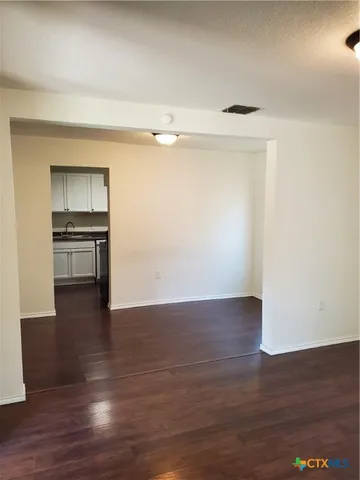 a view of empty room with wooden floor and kitchen