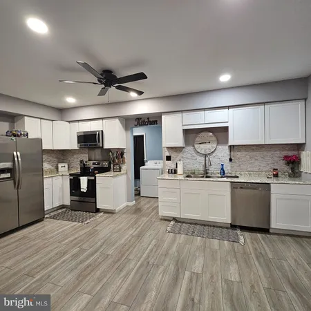 a kitchen with granite countertop a refrigerator oven a sink white cabinets and stainless steel appliances