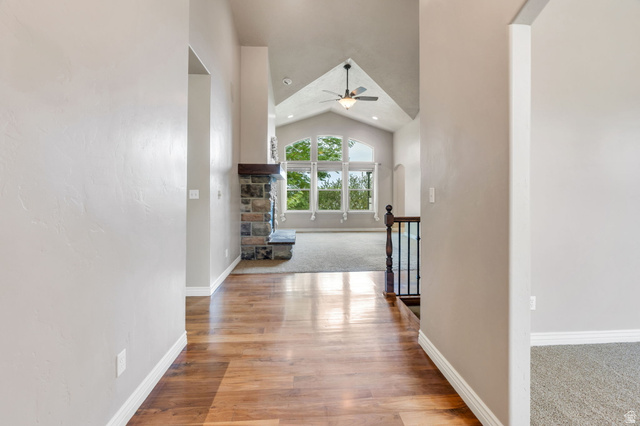 373 East Alexander Drive Elk Ridge, UT 84651 - Photo 12 of 69 Vaulted ceiling with a ceiling fan, stone fireplace with a wood mantel, large arched windows, wood-finish flooring, and a wrought iron railing
