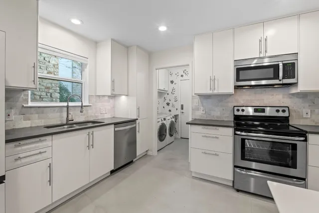 a kitchen with stainless steel appliances granite countertop white cabinets a sink a stove a microwave and a window