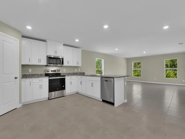 a large white kitchen with stainless steel appliances granite countertop a stove a sink a refrigerator and white cabinets with wooden floor