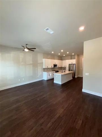 an empty room with wooden floor and kitchen view