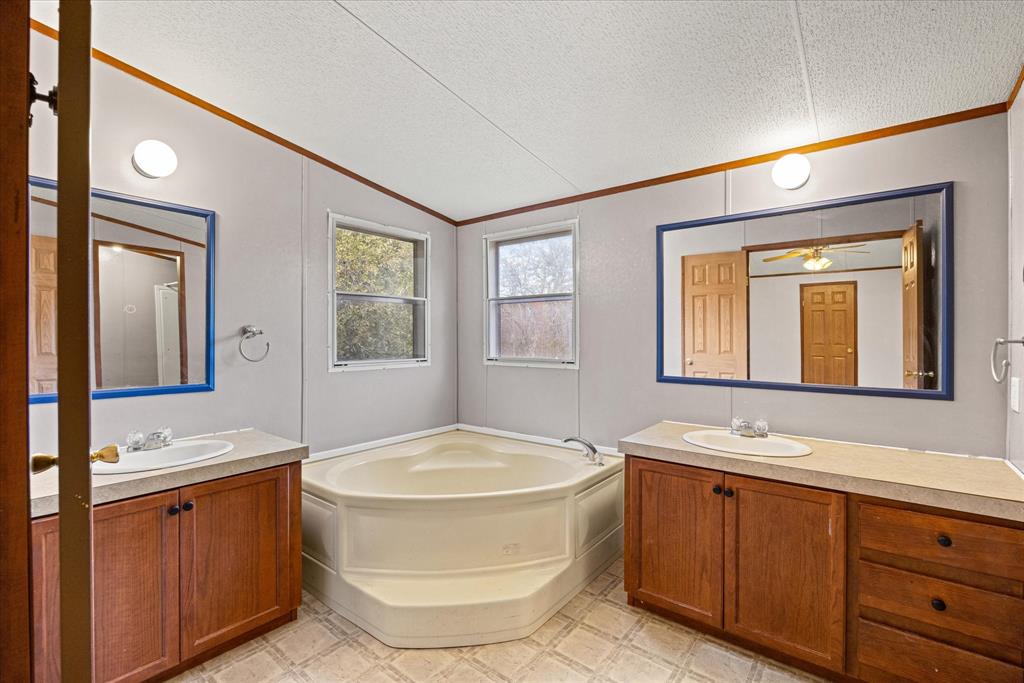 2903 Centaurus Way Granbury, TX 76048 - Photo 26 of 31 Bathroom featuring two vanities, a textured ceiling, a garden tub, crown molding, and lofted ceiling