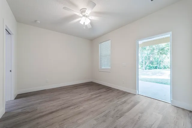 an empty room with wooden floor chandelier fan and windows