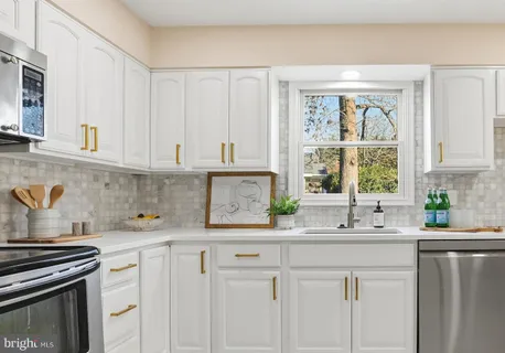a kitchen with stainless steel appliances granite countertop white cabinets a sink and a window