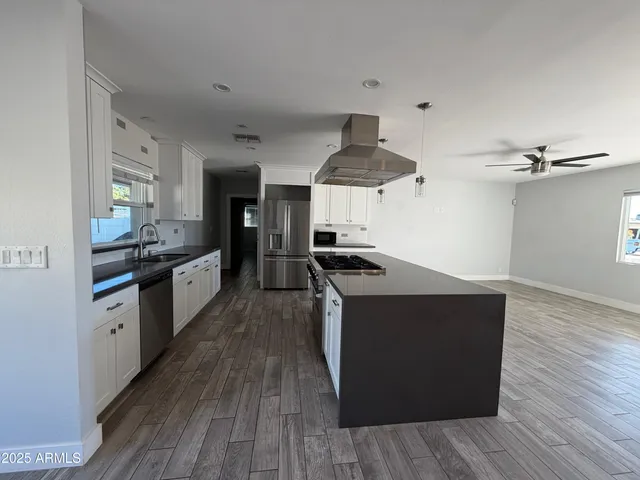 a large kitchen with stainless steel appliances a large counter top a stove and a wooden floors