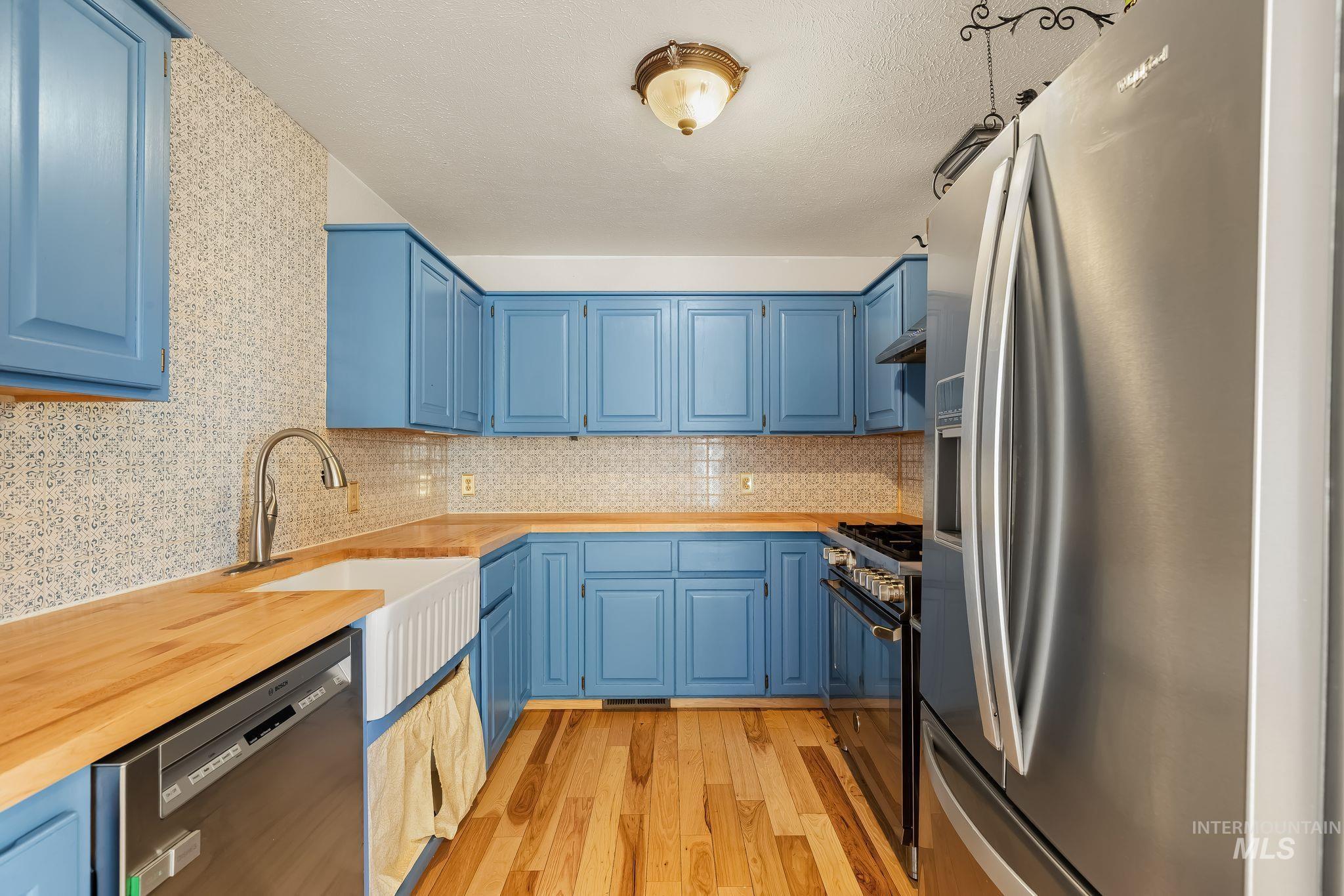 1820 Winchester Road Winchester, ID 83555 - Photo 14 of 50 Kitchen featuring blue cabinetry, light wood-finish countertops, stainless steel appliances, and a farmhouse sink