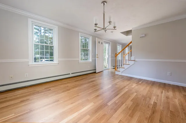 a view of an empty room with wooden floor fridge and a window