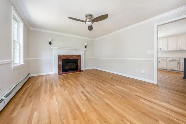 an empty room with wooden floor a ceiling fan a fireplace and windows