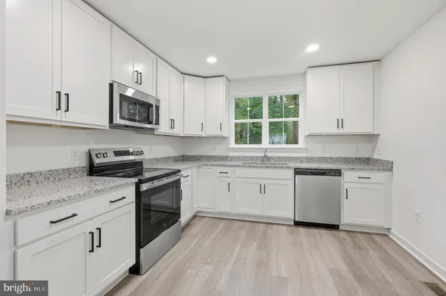 a kitchen with granite countertop white cabinets a window a sink and a oven