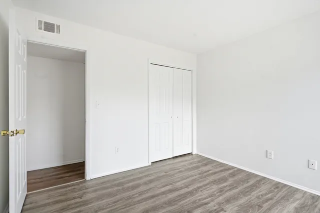a view of an empty room with wooden floor and closet