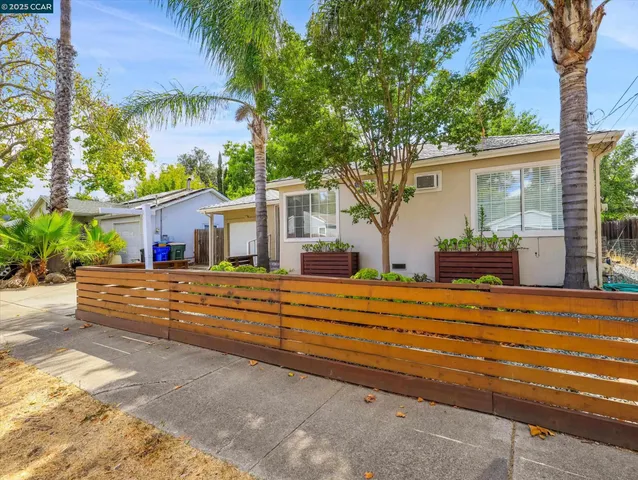 a front view of a house with large trees and plants