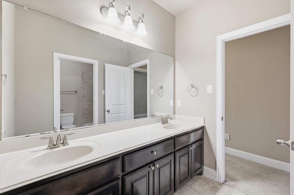 768 Huntingdon Street Coppell, TX 75019 - Photo 28 of 37 Clean and functional bathroom vanity with two sinks, dark wood cabinetry, neutral flooring, and bright overhead lighting.