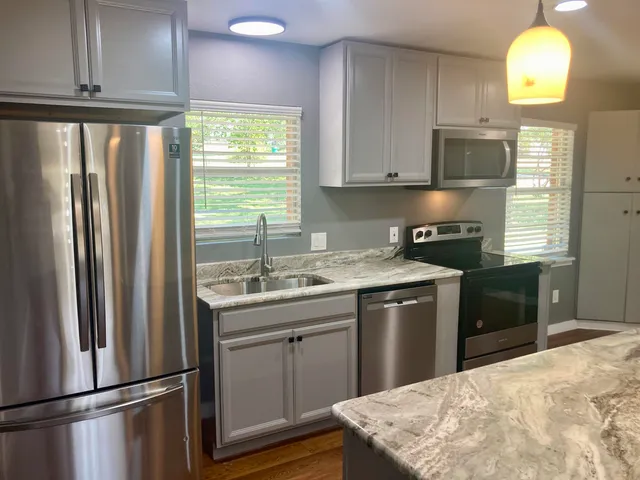 a kitchen with stainless steel appliances granite countertop a refrigerator a sink a stove and a window